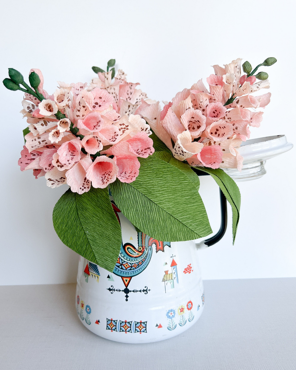 a white vase with pink flowers and green leaves