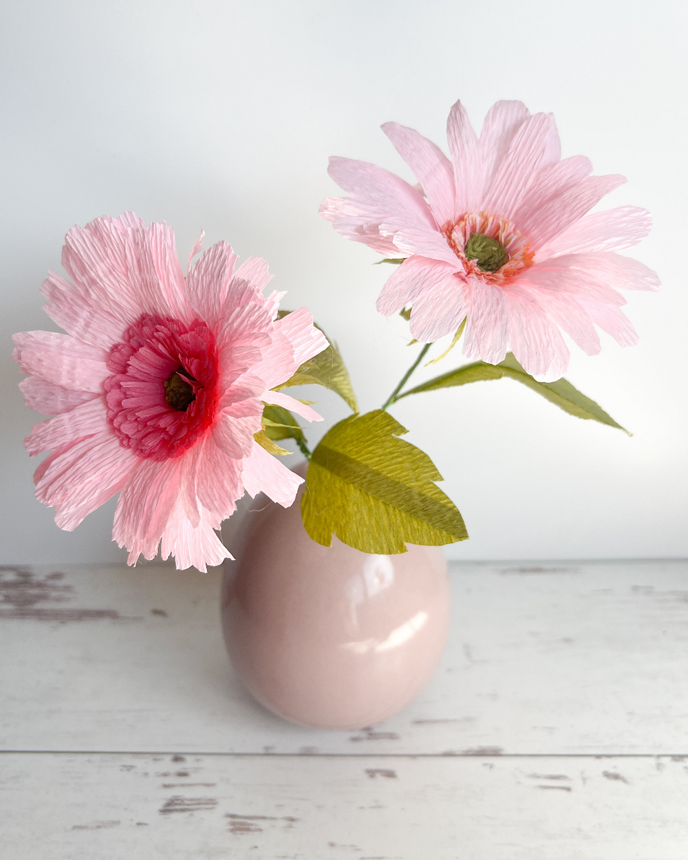 two pink flowers in a pink vase on a white table