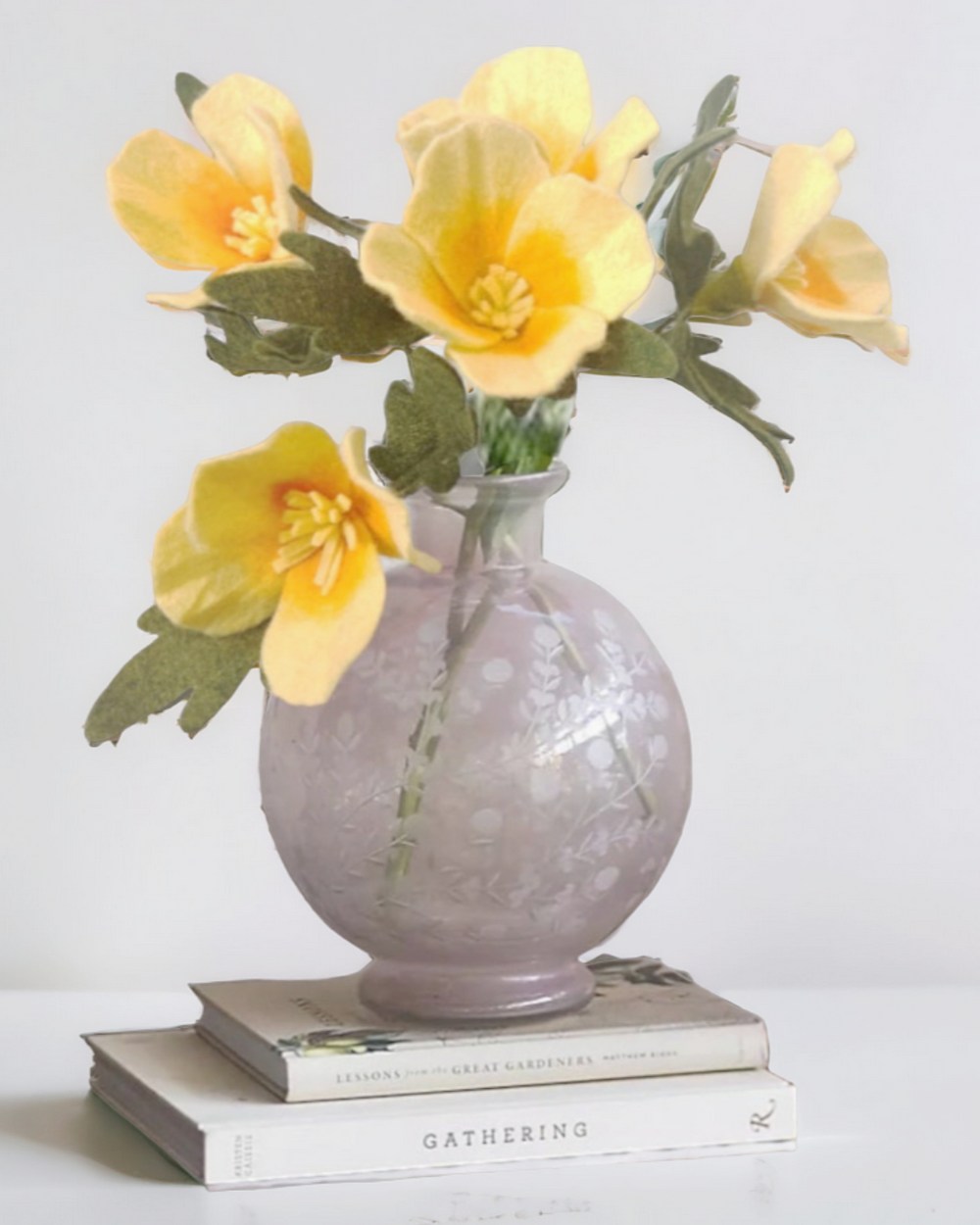 a gray vase with yellow flowers on top of a stack of books