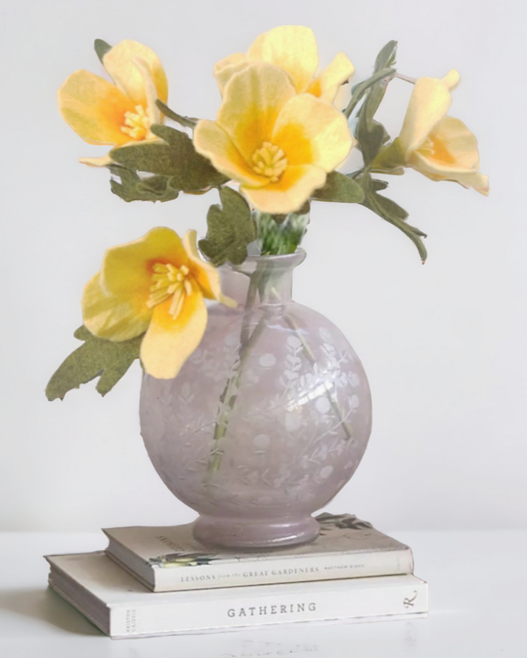 a gray vase with yellow flowers on top of a stack of books
