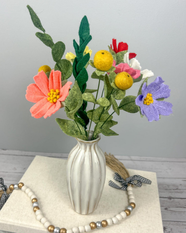 a white vase filled with colorful flowers on top of a table