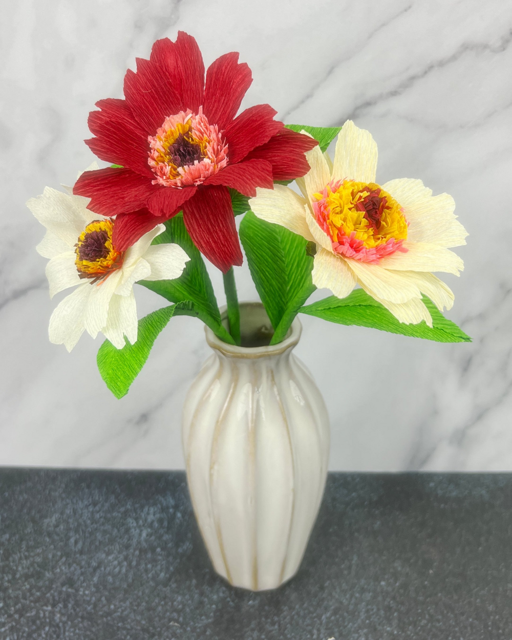 a white vase filled with red and yellow flowers