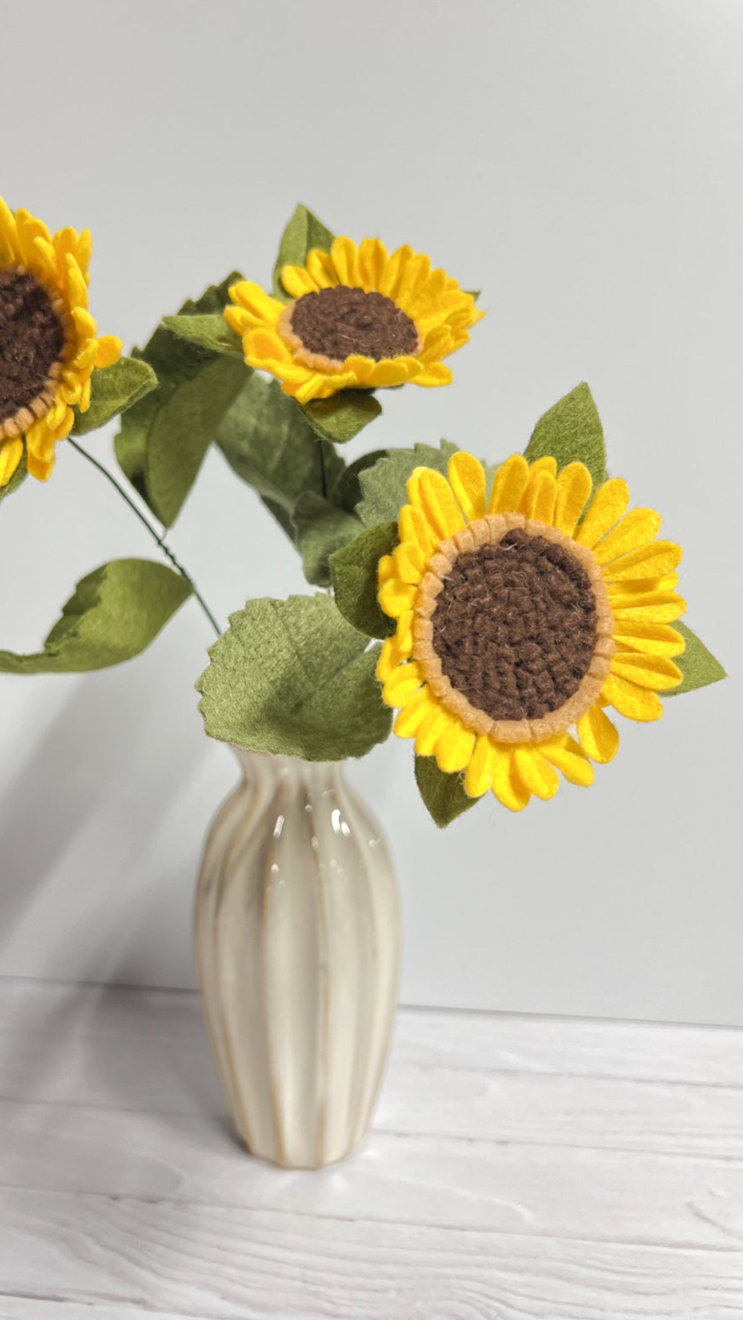 a white vase with three yellow sunflowers in it