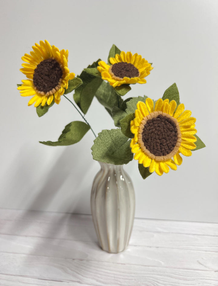 a white vase with three sunflowers in it