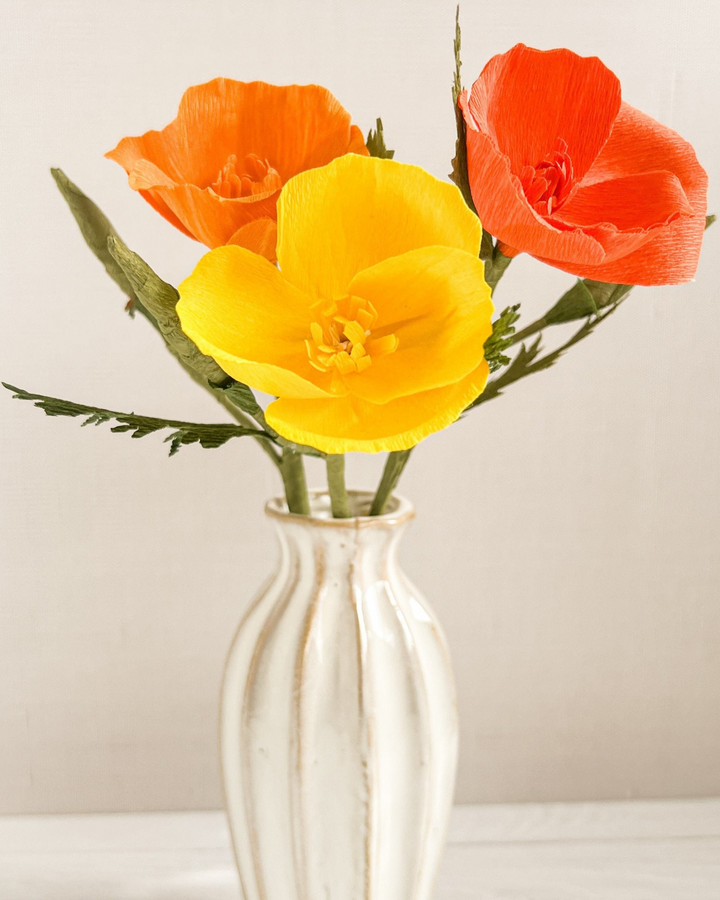 three orange and yellow flowers in a white vase