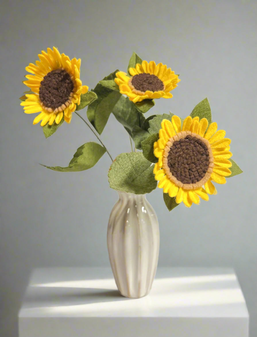 a white vase with three sunflowers in it