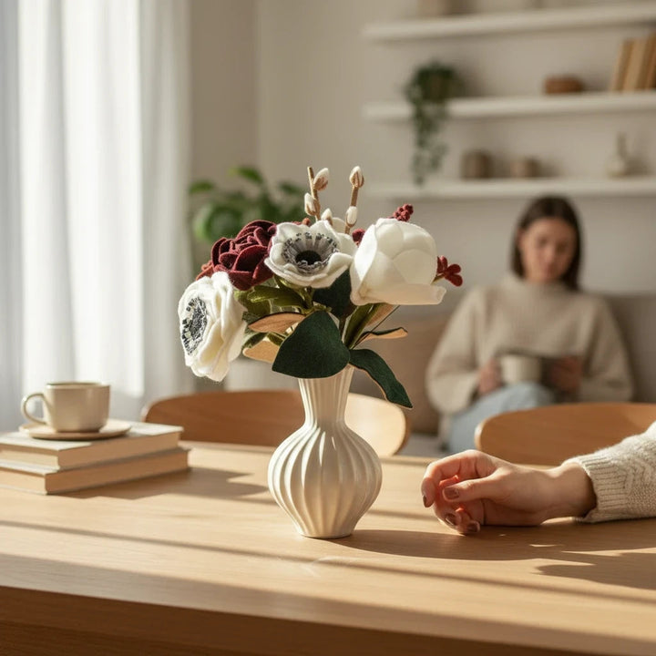 Melly Meier Botanicals handcrafted felt flower bouquet in deep burgundy and white on a wooden table in a cozy room.