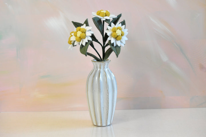 Melly Meier Botanicals handcrafted felt edelweiss stem with four white and yellow wool flowers in a fluted vase.