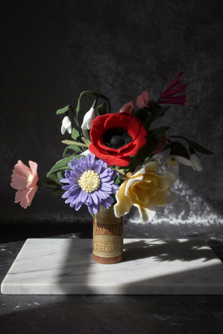 Melly Meier Botanicals bouquet of felt flowers including a red poppy, purple daisy, yellow rose, pink blossom, and snowdrops.